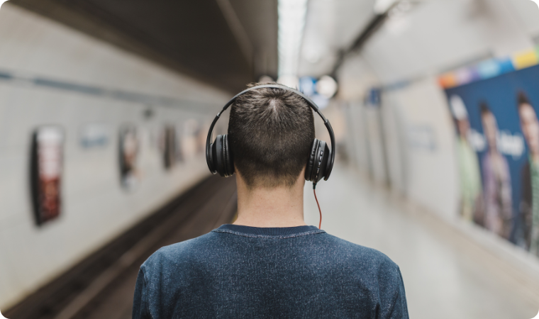 man listening to music through headphones at train station